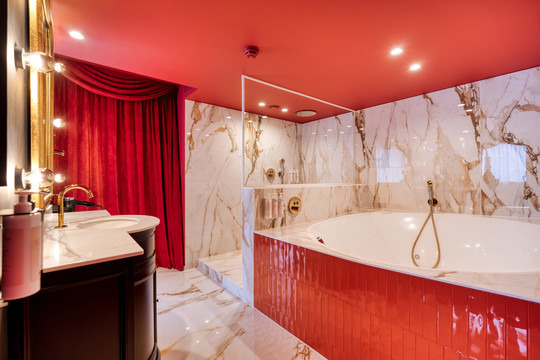 Profitez d’un moment de détente dans la salle de bain luxueuse de la Suite Cabaret Rouge à Liège, équipée d’un jacuzzi privatif, d’une douche à l’italienne et de finitions en marbre pour un confort absolu.