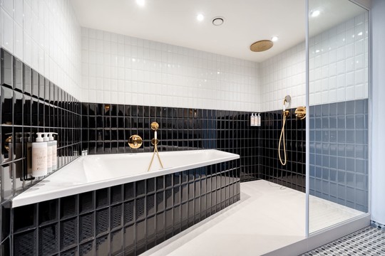 Salle de bain luxueuse de la Suite Gatsby avec bain à bulles et douche à l’italienne, marbre raffiné et éclairage tamisé pour une expérience bien-être à l’hôtel Van der Valk Liège Congrès.